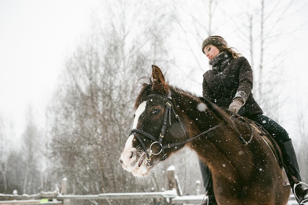 Photo low angle view of beautiful woman riding horse on snow covered field