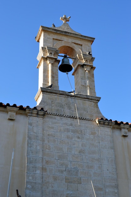 Low angle view of bell hanging on arch with cross on top against clear sky