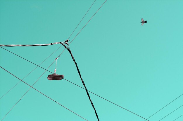 Photo low angle view of bird flying over cables against clear blue sky