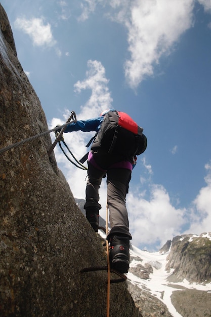 Foto vista a bassa angolazione di un ragazzo che si arrampica su una montagna contro il cielo