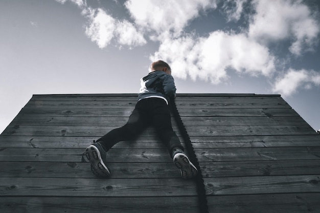 Photo low angle view of boy sitting on wood against sky