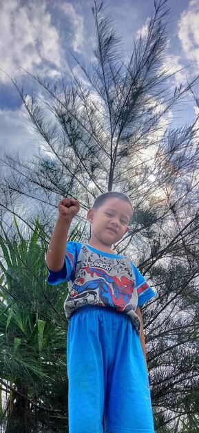 Low angle view of boy standing by tree against sky