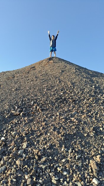 Foto vista ad angolo basso di un ragazzo in piedi su una collina contro un cielo blu limpido