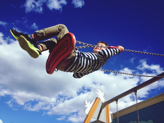 Foto vista a basso angolo di un ragazzo che si oscilla contro il cielo blu al parco giochi