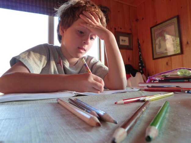 Photo low angle view of boy writing on book at table