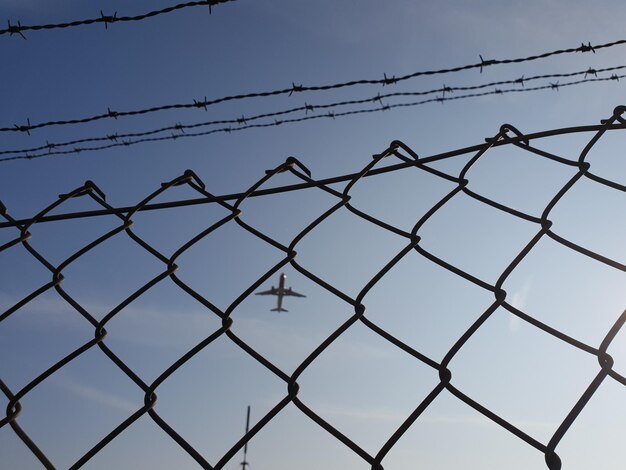 Low angle view of chainlink fence against airplane