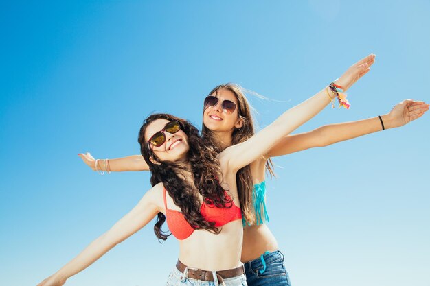 Photo low angle view of cheerful friends with arms outstretched wearing sunglasses against sky during summer