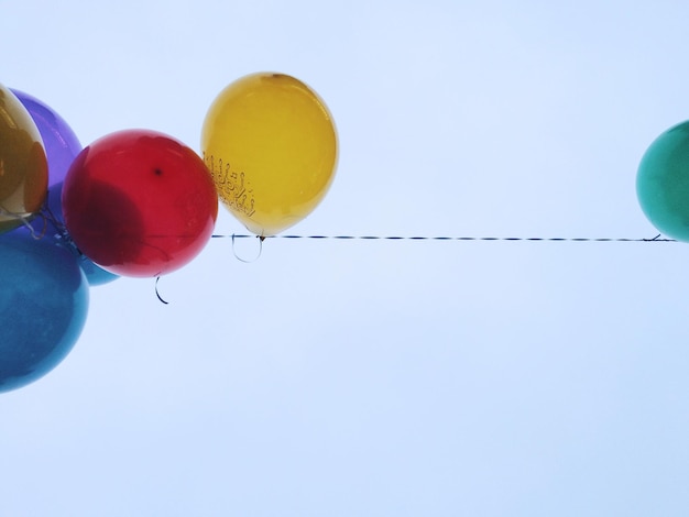 Foto vista a basso angolo di palloncini colorati appesi a una corda contro il cielo