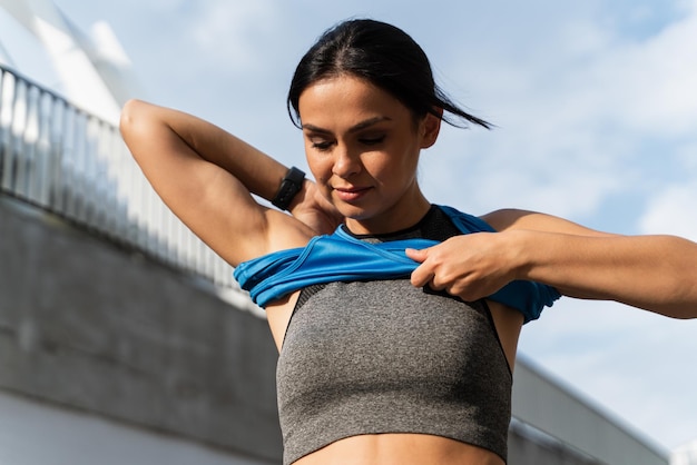 Low angle view of the concentrated woman changing her clothes near the stadium before the training Brunette girl puts on her tshirt