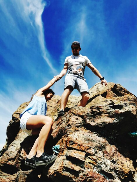 Low angle view of couple hiking on rock formation against blue sky