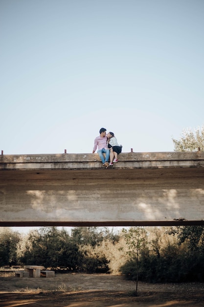 Photo low angle view of couple sitting on bridge against clear sky