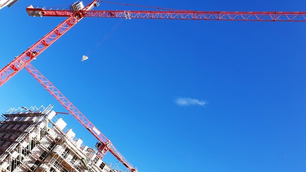 Low angle view of crane by building against clear blue sky