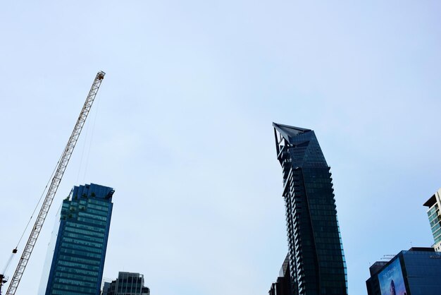 Low angle view of crane by building against sky