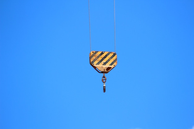 Low angle view of crane hanging against clear blue sky