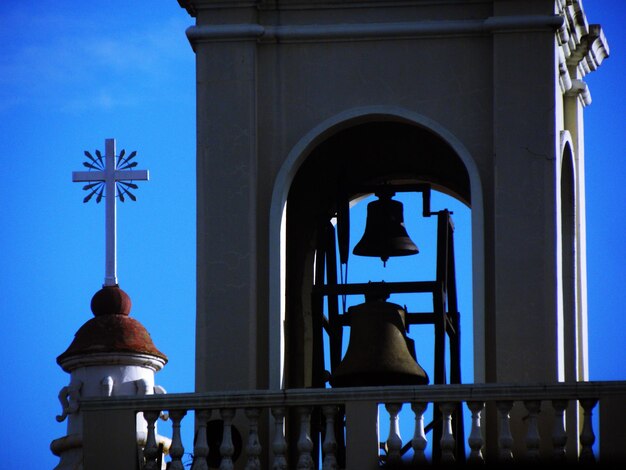 Low angle view of cross against blue sky and building