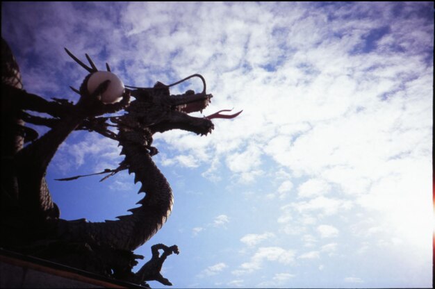 Low angle view of dragon statue against cloudy sky