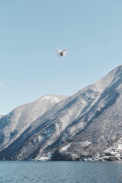 low angle view of drone airplane flying over lake by mountains against sky