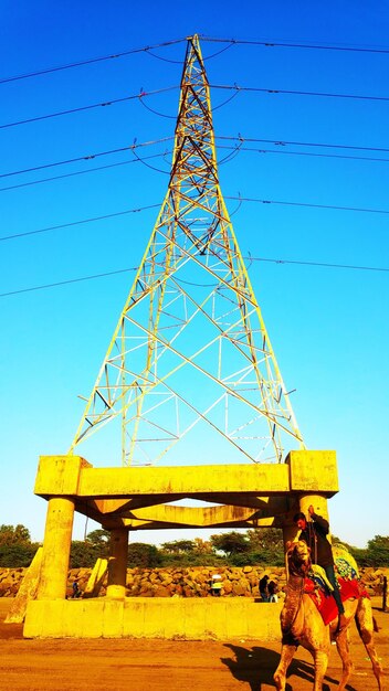 Low angle view of electricity pylon against clear blue sky