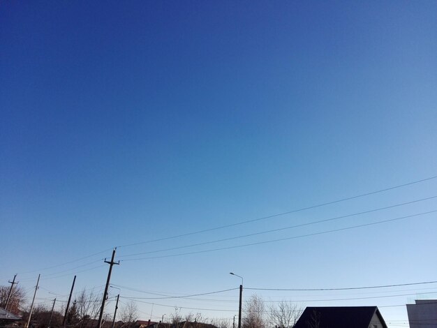 Low angle view of electricity pylon against clear blue sky