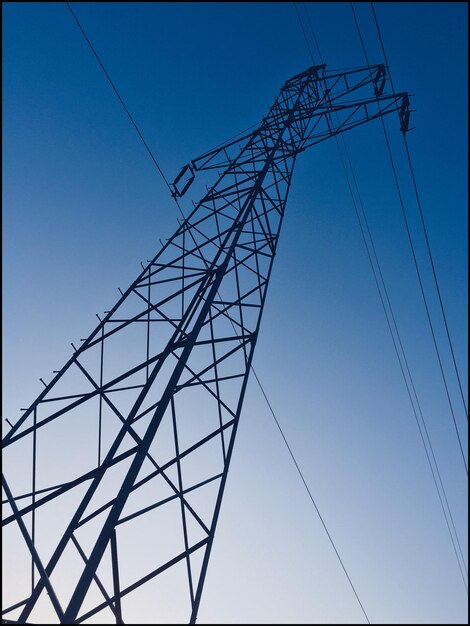 Low angle view of electricity pylon against clear blue sky