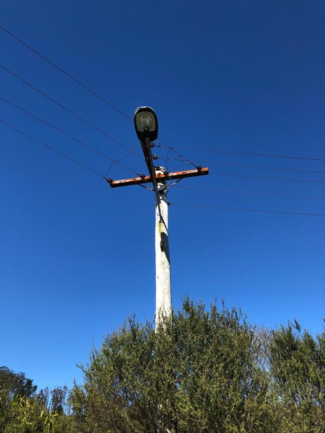 Low angle view of electricity pylon against clear blue sky