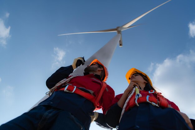 Photo low angle view of engineers standing in front of a wind turbine using the walkie talkie to communicate with coworkers