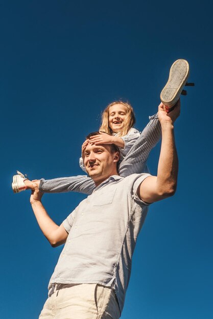 Low angle view of father carrying daughter against clear blue sky