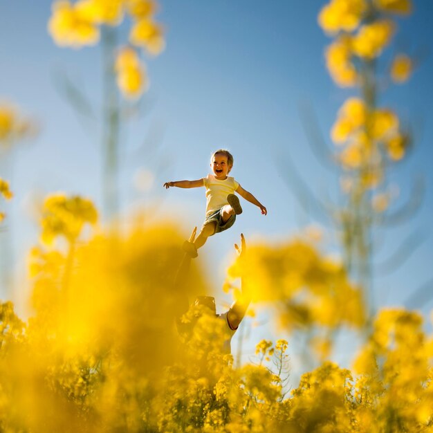 Low angle view of father holding son amidst yellow flowering plant against sky