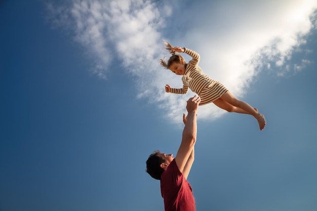 父が娘を空に投げかける低角度の写真