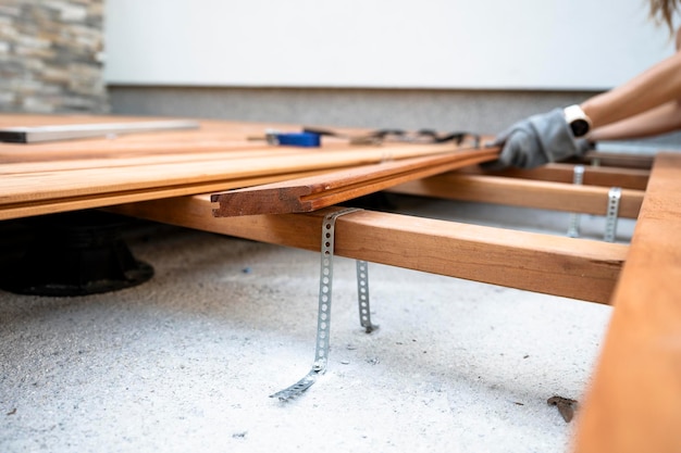 Foto vista ad angolo basso di mani femminili che posizionano una tavola di legno su una costruzione di fondazione per un patio.