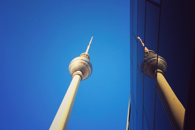Low angle view of fernsehturm by modern building against clear blue sky