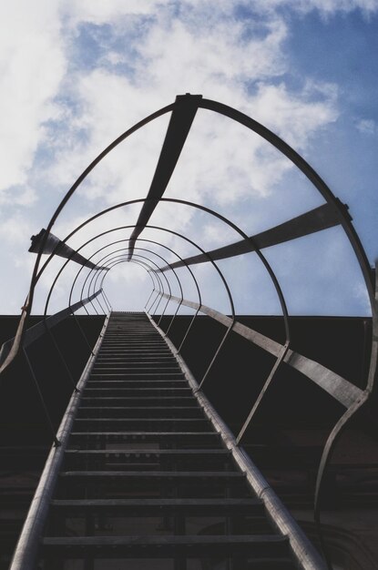 Low angle view of fire escape ladder against cloudy sky