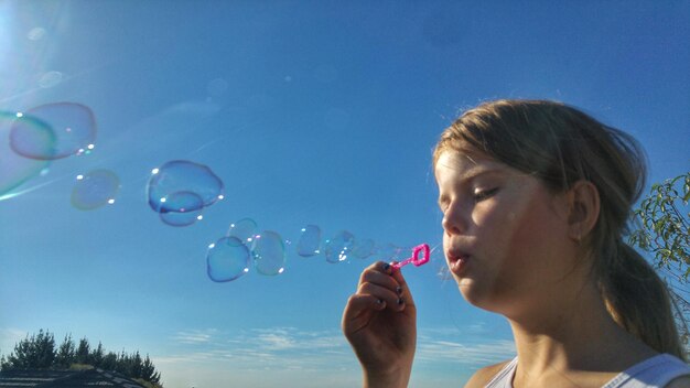 Низкий угол зрения девушки, дующей пузырьки с помощью палочки