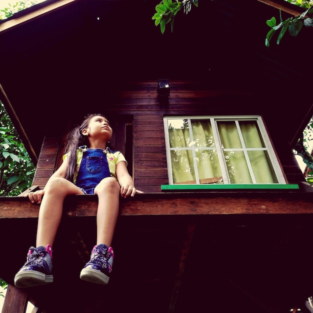 Low angle view of girl sitting on built structure