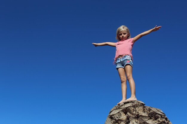 Foto vista a basso angolo di una ragazza in piedi contro un cielo blu limpido