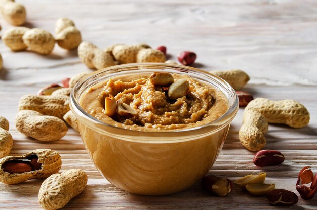 Low angle view at glass bowl with peanut butter on white wooden table. Healthy eating concept