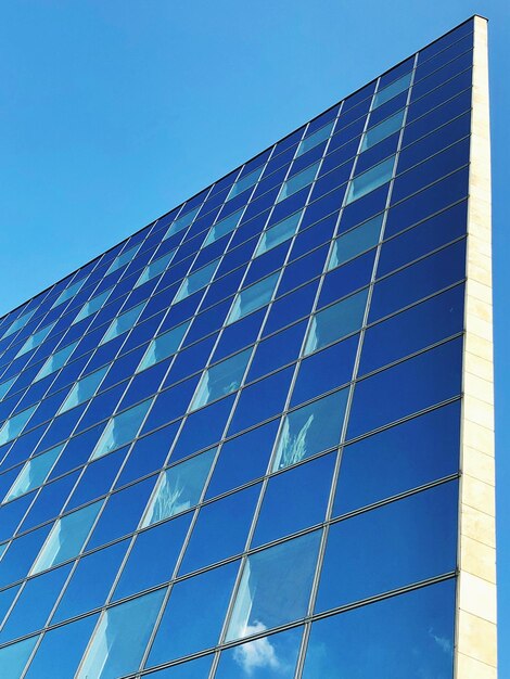 Low angle view of glass building against clear blue sky