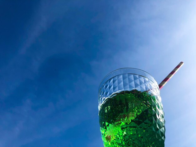 Low angle view of glass of drink against blue sky