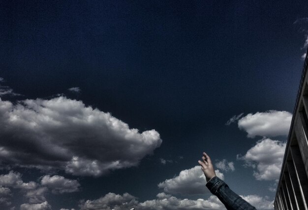 Vista a basso angolo della mano contro un cielo nuvoloso