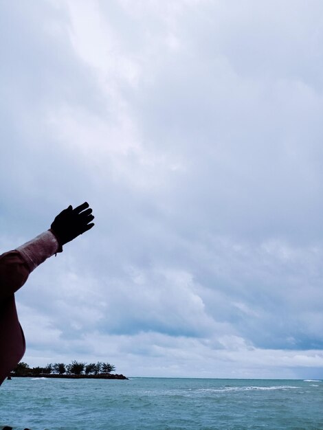 Low angle view of hands over sea against sky