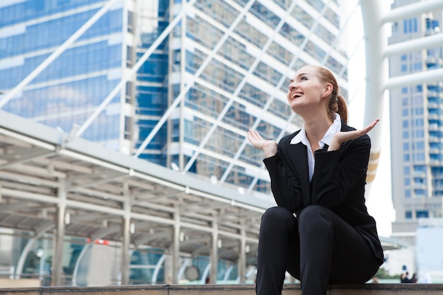 Photo low angle view of happy businesswoman sitting on steps in city