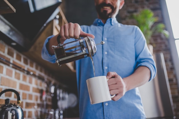 Vista ad angolo basso dell'uomo felice che versa il caffè nella tazza al mattino nell'immagine ritagliata della cucina