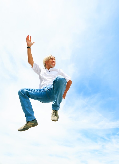 Low angle view of happy mature woman jumping against cloudy sky