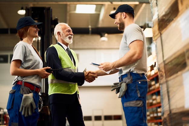 Foto inquadratura dal basso di felice senior manager che stringe la mano con un lavoratore mentre visita un magazzino industriale