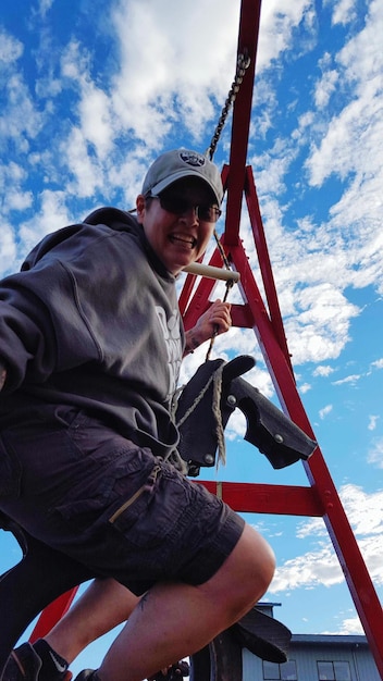 Low angle view of happy woman hanging on zip line against sky