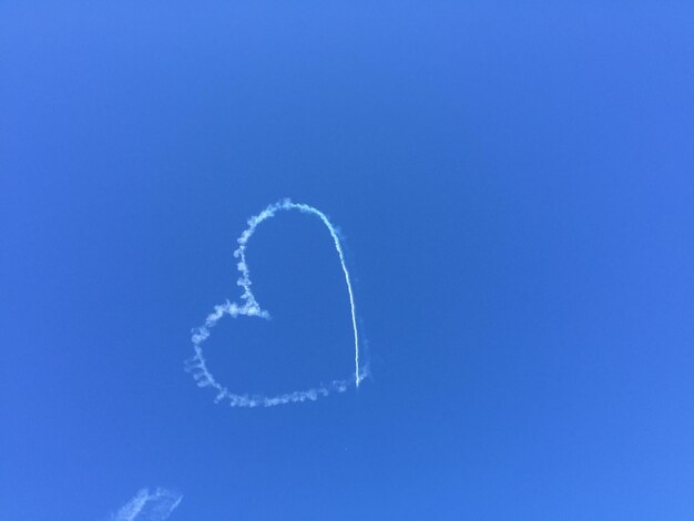 Low angle view of heart shape made with vapor trail against clear blue sky