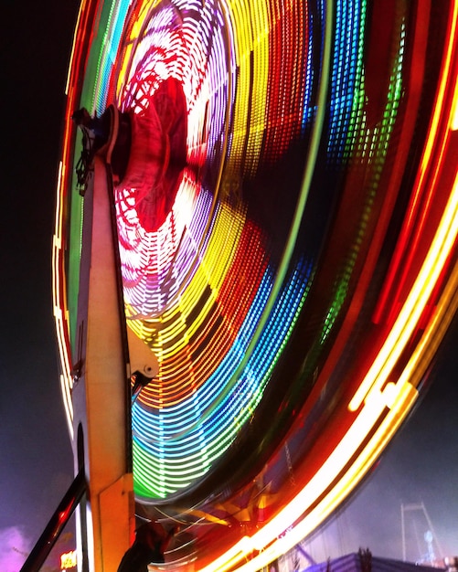 Low angle view of illuminated ferris wheel spinning at night