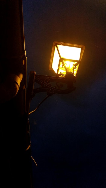 Low angle view of illuminated lamp mounted on wall against sky at night