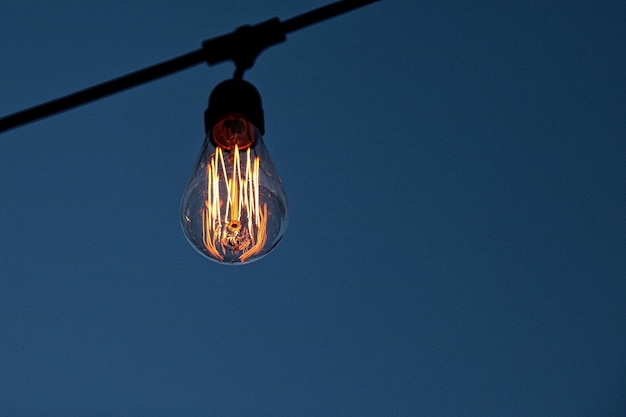 Foto vista a basso angolo di una lampadina illuminata contro un cielo blu limpido
