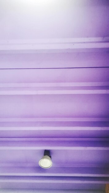 Low angle view of illuminated light bulb on purple wall